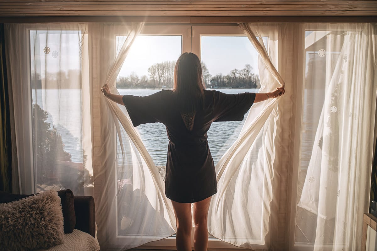Back view of woman in bathrobe opening curtains and looking out